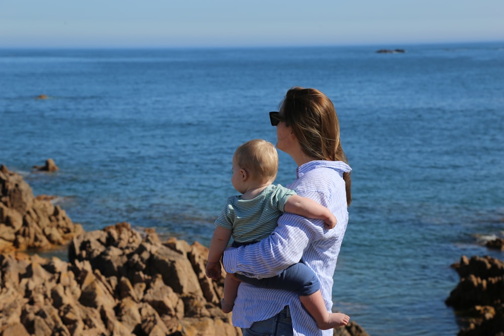 a woman holding a baby near the ocean