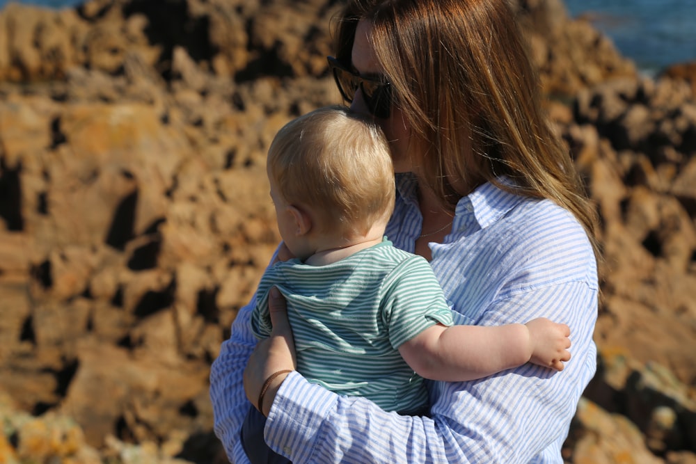 a woman holding a baby on a rocky beach