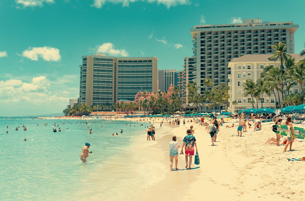 a group of people walking along a beach next to tall buildings