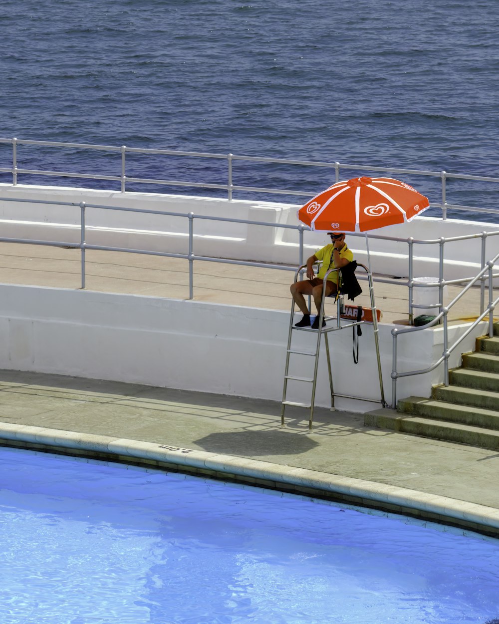 a man sitting under an umbrella next to a swimming pool