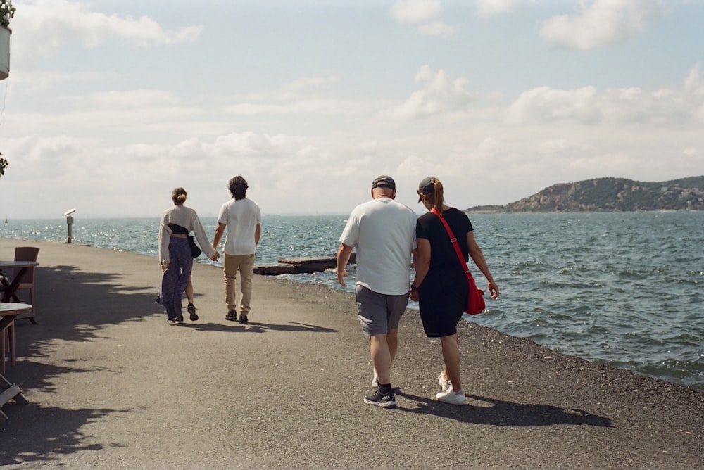 a group of people walking along a pier next to the ocean