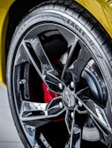A close-up view of a car tire with a glossy black alloy wheel. The tire has the word 'Eagle' printed on it, and the wheel features a prominent black five-spoke design with a logo in the center. Behind the wheel, a red brake caliper is partially visible.