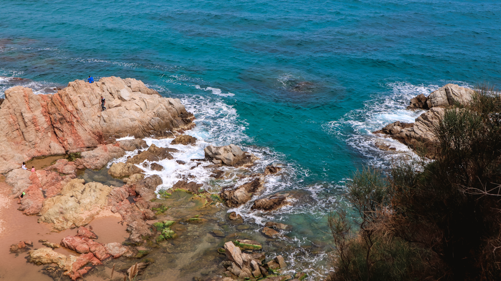 a couple of people standing on top of a cliff next to the ocean