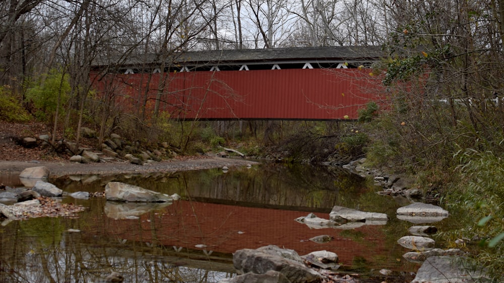 eine rote überdachte Brücke über einen kleinen Bach