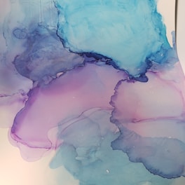 Abstract watercolor artwork featuring soft blending of blue, purple, and pink hues with fluid, overlapping shapes. The colors transition smoothly, creating a sense of calm and movement.