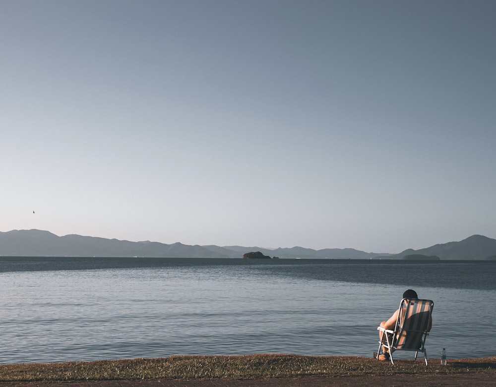 a person sitting in a chair on the shore of a lake