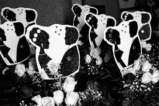 Silhouettes of couples facing each other are set against a pattern of polka dots. The foreground features numerous white roses and baby's breath flowers, creating a romantic and classic atmosphere.