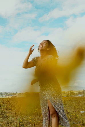 A cheerful woman laughing in a sunny park, dressed in a vivid yellow dress with floral patterns.