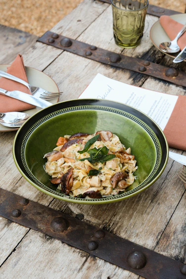 Close-up of a rustic wooden table set with a candlelit plate of handmade pasta and a glass of red wine