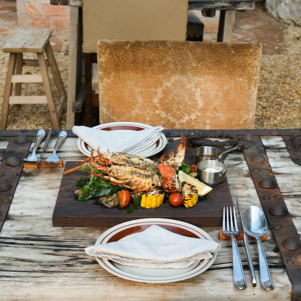 a table set with lobsters, vegetables, and silverware