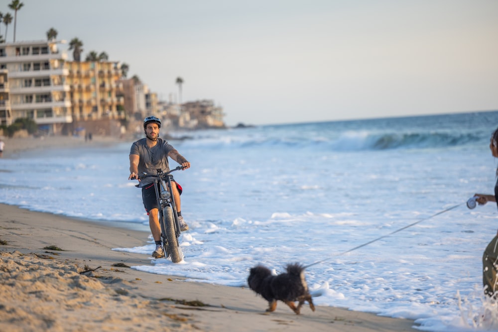 a man riding a bike down a beach next to a dog