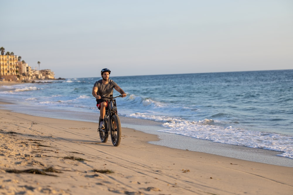 a man riding a bike down a beach next to the ocean