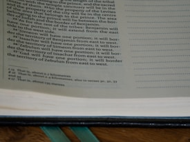 A close-up view of an open book showing printed text on the left page. The text has a formal layout with paragraphs and a section of footnotes at the bottom. The right side of the image shows a portion of blank pages with dotted lines, possibly for writing notes.