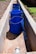 A series of blue perforated buckets placed in a narrow, rectangular concrete channel with sunlight casting shadows. The channel appears to be part of an outdoor setup, possibly for water collection or filtration. The surroundings include some green grass and brown gravel.