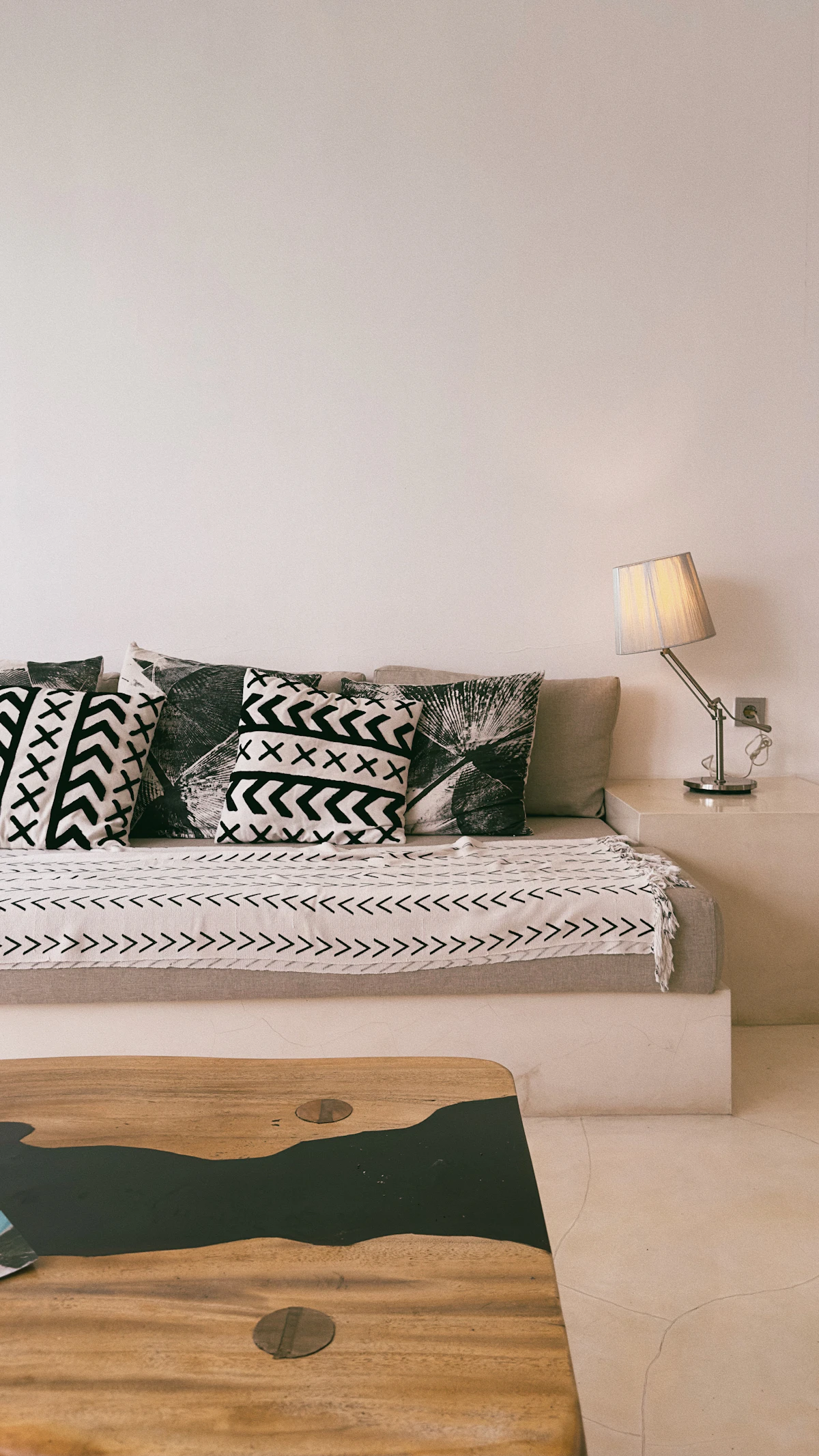 Salon épuré après rénovation : banquette basse et coussins graphiques noir et blanc, table basse bois et résine