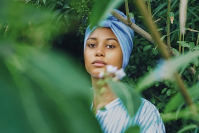 a woman wearing a blue turban standing in front of a bush