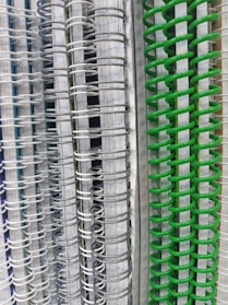Several spiral-bound notebooks are stacked vertically, showcasing a variety of colors in the spiral bindings ranging from white and gray to vivid green. The pages inside have lined paper, creating a neat and organized appearance.