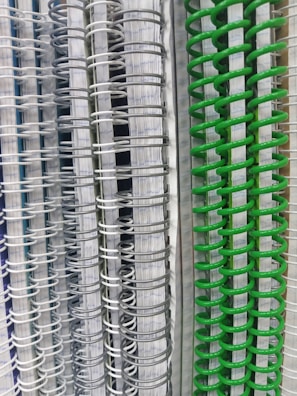 Several spiral-bound notebooks are stacked vertically, showcasing a variety of colors in the spiral bindings ranging from white and gray to vivid green. The pages inside have lined paper, creating a neat and organized appearance.
