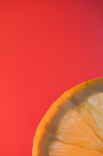 A close-up of a lemon slice with its vibrant yellow color and textured surface, positioned against a bright red background.