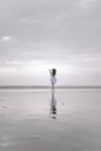 A solitary figure is seen in the distance on a vast, reflective beach, under an expansive, cloudy sky. The scene has a dreamlike and serene quality due to the out-of-focus element.