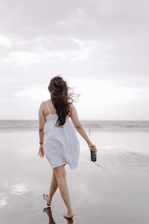 A candid shot of Hollan walking along a beach boardwalk, wearing a flowing white dress and simple leather sandals.