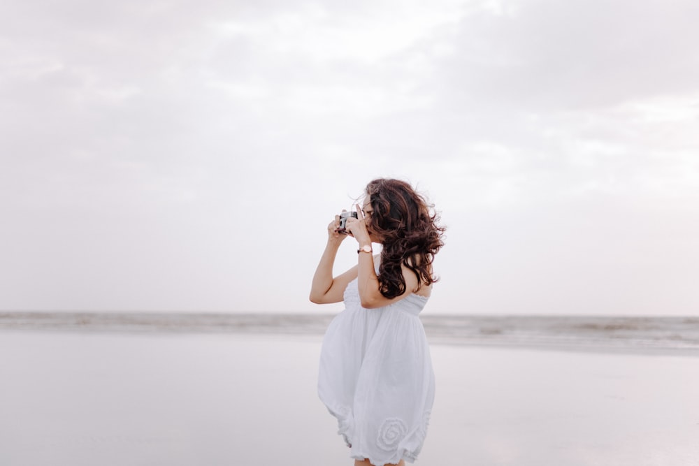 a woman standing on a beach taking a picture of the ocean