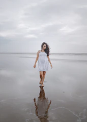 A joyful scene of a woman walking along the shore wearing casual beachwear, with waves gently touching her feet.
