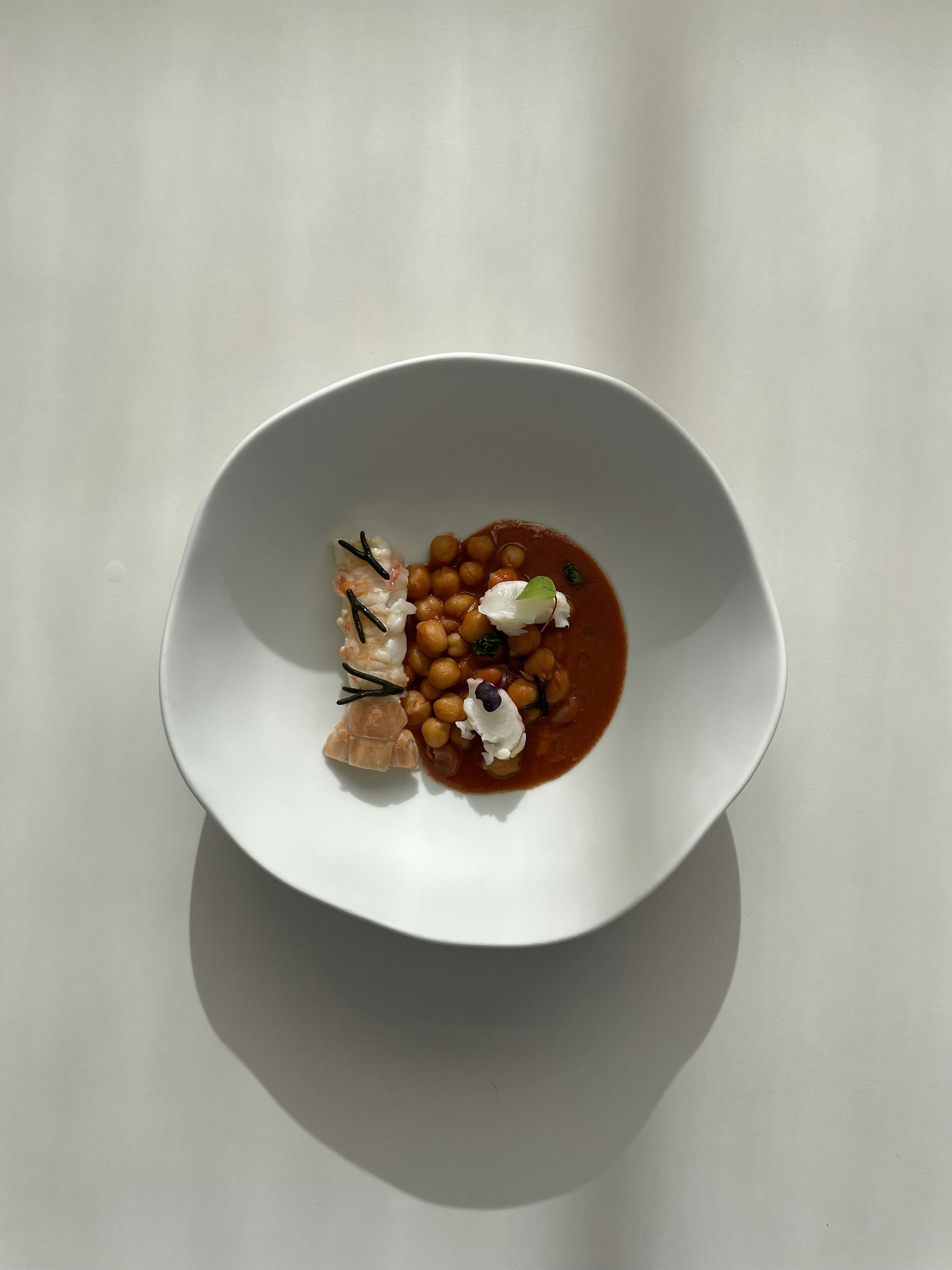 Elegant starter course with lobster bisque in white bowl, fine dining presentation in dim restaurant