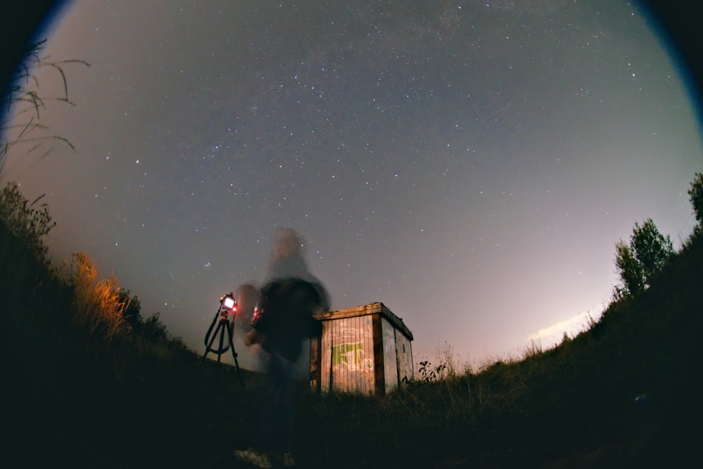 Un hombre de pie junto a una pequeña casa bajo un cielo nocturno