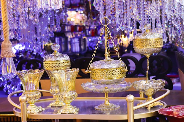 Ornate glass and gold decorative items are arranged on a tray, surrounded by crystal chandeliers and a warm ambient glow. The luxurious design features intricate details and craftsmanship.
