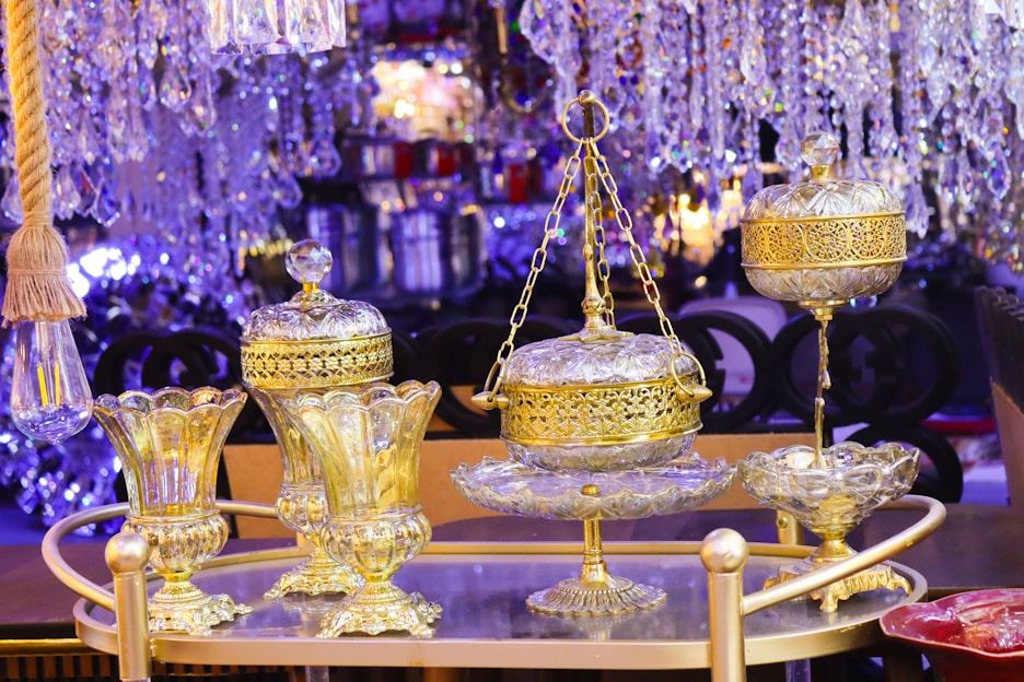 Ornate glass and gold decorative items are arranged on a tray, surrounded by crystal chandeliers and a warm ambient glow. The luxurious design features intricate details and craftsmanship.
