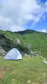 A man setting up a tent on a grassy plateau surrounded by rolling hills and wildflowers.