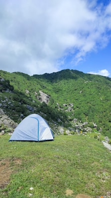 A man setting up a tent on a grassy plateau surrounded by rolling hills and wildflowers.