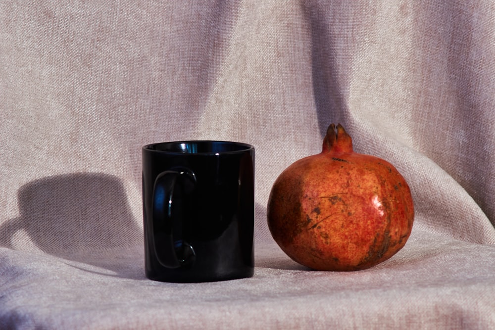 a black coffee mug next to a red pomegranate