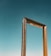 A large, ornate rectangular frame structure made of metal with intricate patterns stands against a clear blue sky.