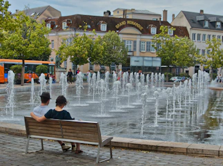 two people sitting on a bench in front of a fountain