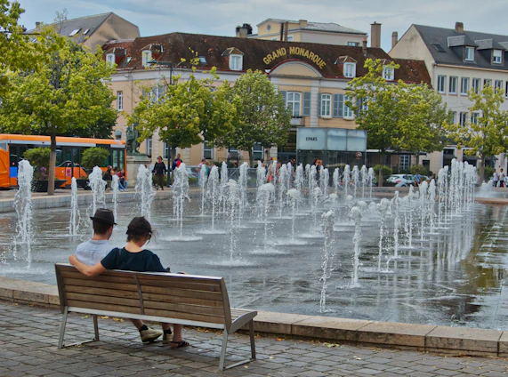 two people sitting on a bench in front of a fountain