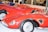 Several vintage red sports cars with sleek designs are parked closely together. The cars feature low profiles, prominent headlights, and wire-spoke wheels. The glossy finish highlights the elegant curves and aerodynamic shapes of the vehicles.