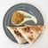 A gray plate features a colorful quinoa salad portion accompanied by a creamy sauce. Next to it are two slices of browned tortilla, likely filled with ingredients.
