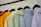 A row of colorful hoodies displayed on black hangers. The hoodies are in shades of orange, yellow, green, blue, and lavender, arranged in a gradient order.