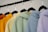 A row of colorful hoodies displayed on black hangers. The hoodies are in shades of orange, yellow, green, blue, and lavender, arranged in a gradient order.