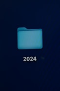 A computer screen displays a digital folder with a light blue color. Below the folder, the number '2024' is prominently shown in white text.
