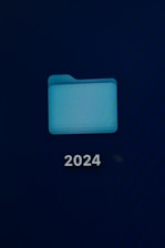 A computer screen displays a digital folder with a light blue color. Below the folder, the number '2024' is prominently shown in white text.