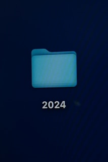 A computer screen displays a digital folder with a light blue color. Below the folder, the number '2024' is prominently shown in white text.
