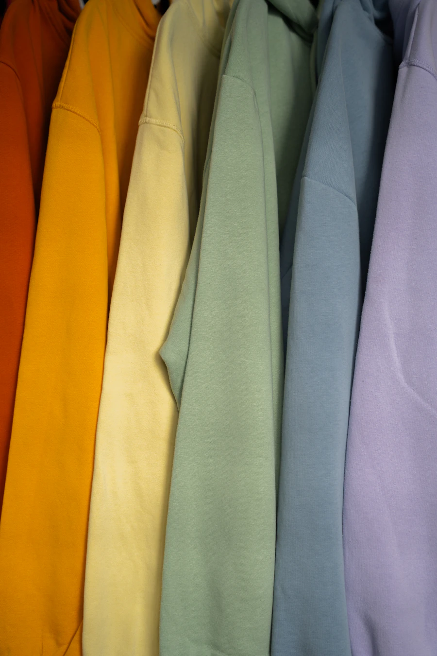 A row of plain sweatshirts in orange, yellow, green, blue and lilac on a rail