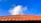 A traditional terracotta roof is visible against a vibrant blue sky with a few fluffy white clouds. The roof has a distinct pattern with uniformly arranged tiles and a decorative finial at the top center.