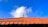 A traditional terracotta roof is visible against a vibrant blue sky with a few fluffy white clouds. The roof has a distinct pattern with uniformly arranged tiles and a decorative finial at the top center.