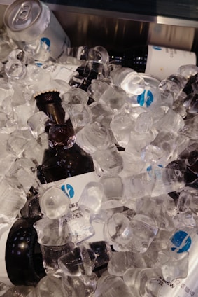 Several bottles and cans of beverages are submerged in a large quantity of clear ice cubes.