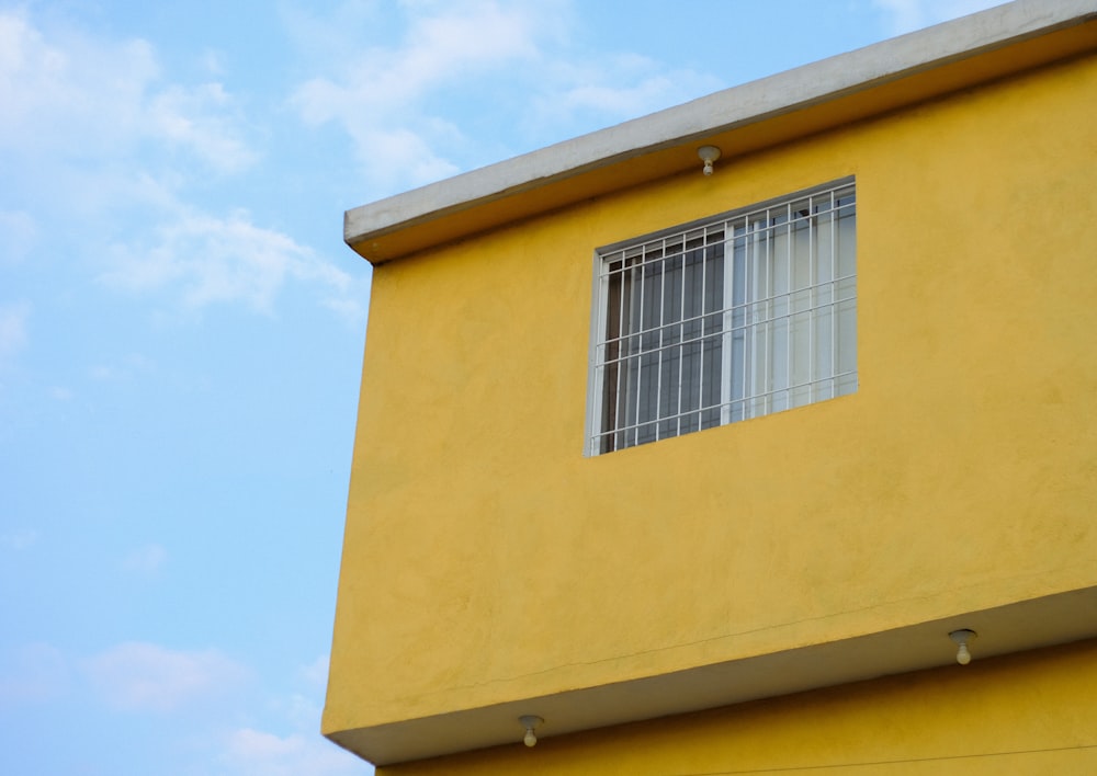 ein gelbes Gebäude mit einem Fenster und einem Himmelshintergrund