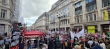 A large crowd of people gathered on a city street, holding signs and banners advocating for the freedom of Palestine. The street is surrounded by tall buildings, including the University of Westminster. A red canopy labeled 'Socialist Party' is prominent among the crowd.